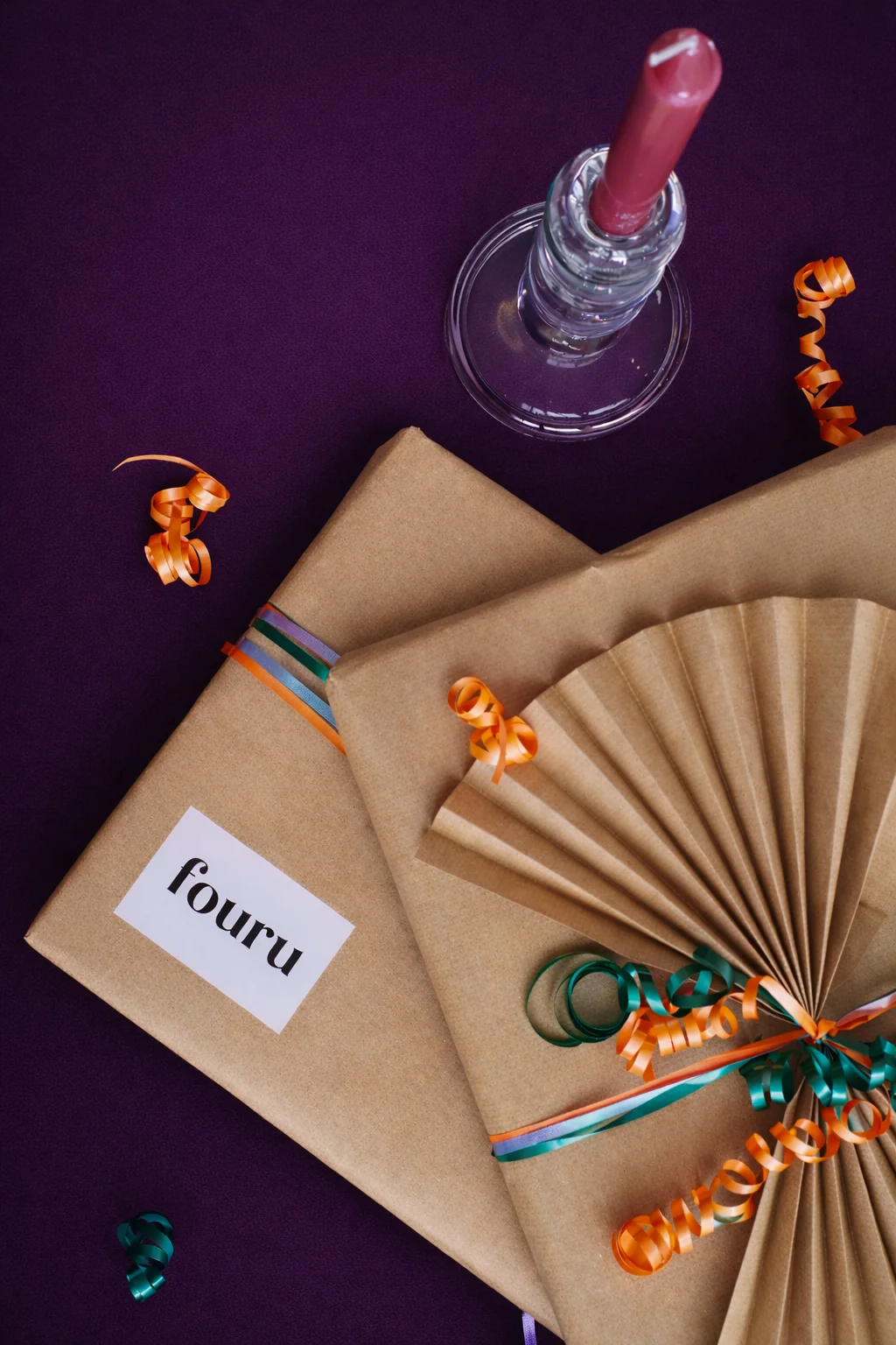 Relatiegeschenk in kraftpapier met een FOURU-label, oranje lint en een waaier op een paarse achtergrond